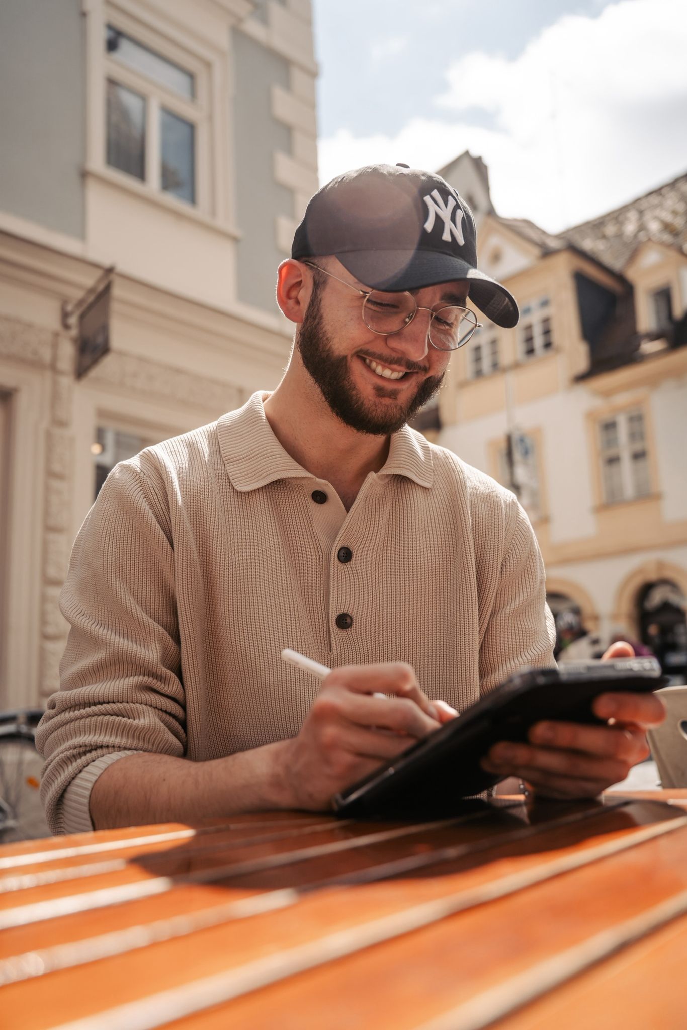 Junger Mann mit Brille und Mütze, der lächelnd auf ein Tablet schaut - symbolisiert Hoffnung und Verbindung